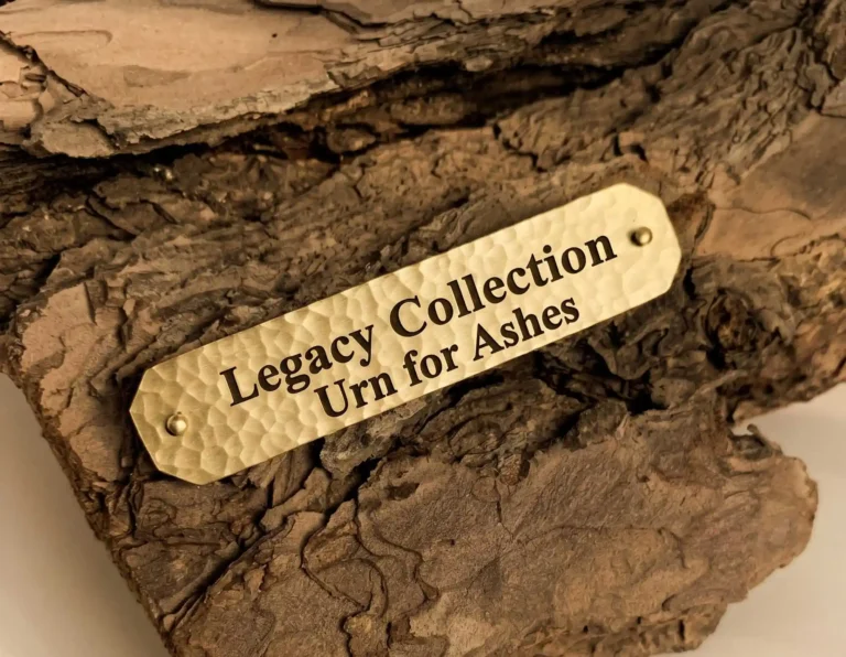 A metal nameplate with the inscription Legacy Collection Urn for Ashes resting on a wood texture