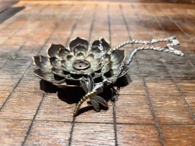 Silver dragonfly cremation necklace for ashes resting on a wooden surface from Royal Memorials
