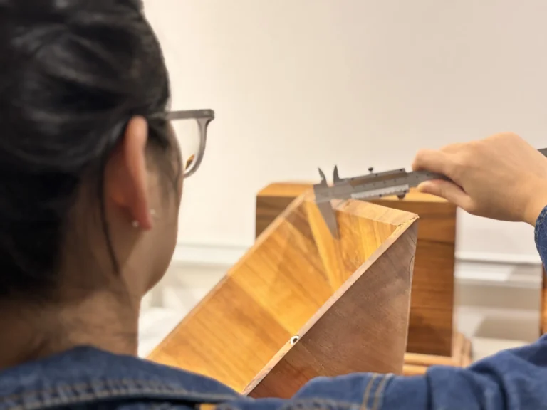 Person using a vernier caliper to measure the external dimensions of a wooden cremation urn