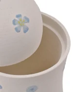 Close-up of off-white ceramic pet urn showing subtle surface texture, hand-painted blue circles, and five-petal flowers with yellow centers