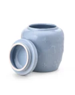 Light blue ceramic pet urn with removable lid placed beside the open top, showing the interior and raised bone and paw details