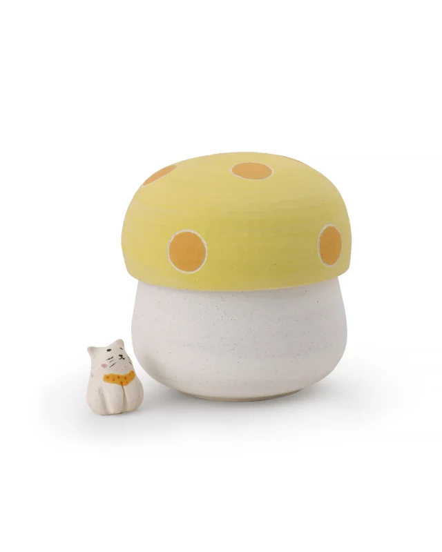 Mushroom ceramic keepsake urn with a yellow spotted lid and speckled cream body, shown beside a small cat figurine