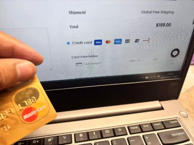 A hand holding a Mastercard in front of the Royal Memorials credit card checkout form